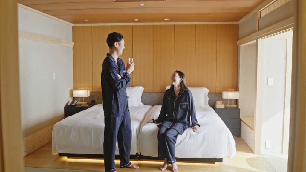 A male and female guest relaxing in a traditional Japanese-style room at Hanakohro, wearing BAKUNE pajamas.