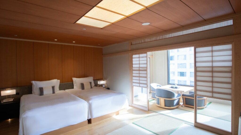 A scene of the Japanese Suite room on the Takanawa Hanakohro with twin beds, a table, and chairs.