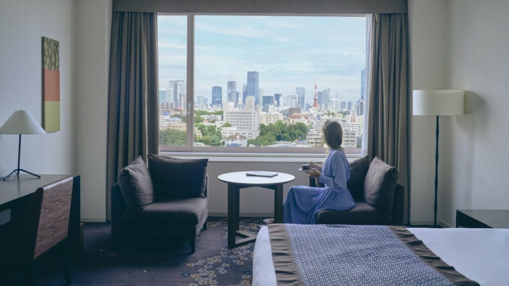 酒店客房内,一位女性宾客坐在窗边的椅子上,欣赏窗外的景色。