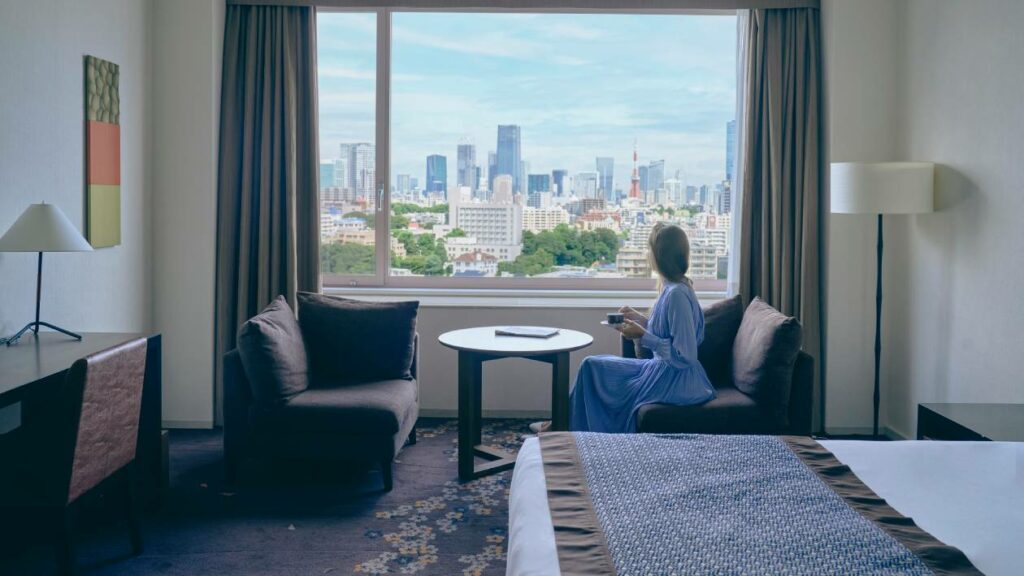 A female guest sitting in a chair by the window of a hotel room, looking at the view outside.