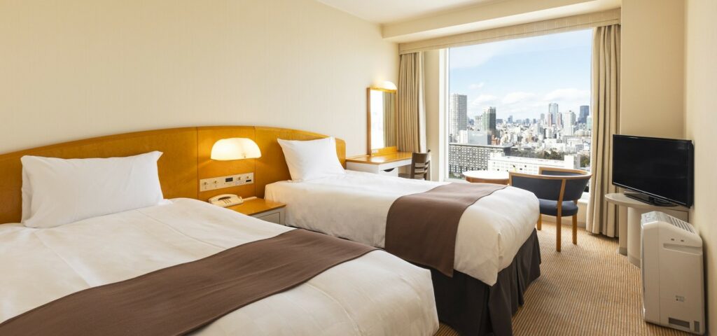 Photo of the twin room during the daytime. You can enjoy views of the city from the large windows.